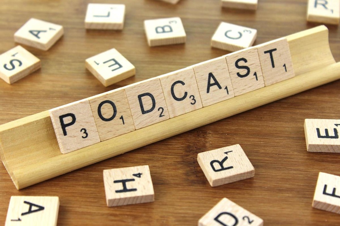 Ordet PODCAST stavat med Scrabble-brickor på ett träbord.